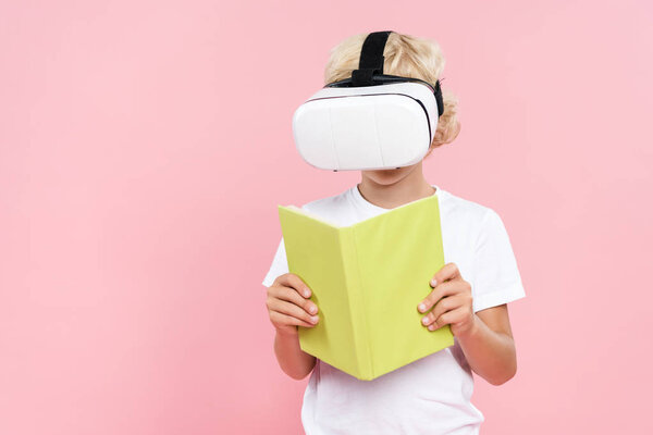 kid with virtual reality headset reading book isolated on pink