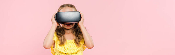 panoramic shot of smiling kid with virtual reality headset isolated on pink