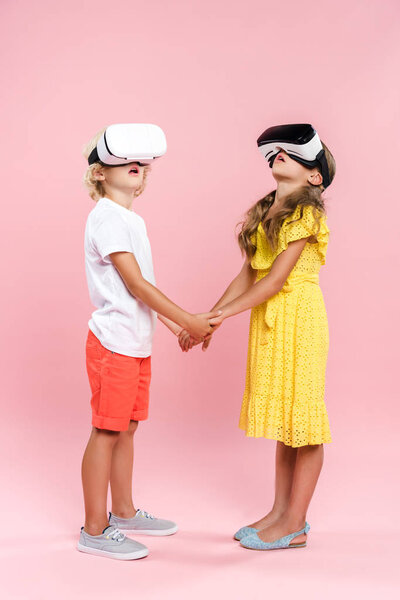 shocked kids with virtual reality headset holding hands on pink background 