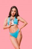 sexy Mädchen im Badeanzug steht mit der Hand in der Hüfte und hält süße Schokoladenriegel isoliert auf rosa 