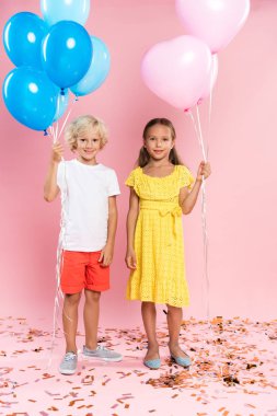 Gülümseyen ve pembe arka planda balon tutan sevimli çocuklar. 