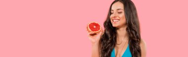Pembe üzerine izole edilmiş greyfurtun yarısını tutan mutlu kadının panoramik görüntüsü. 