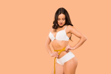 beautiful woman in underwear measuring waist isolated on beige  clipart