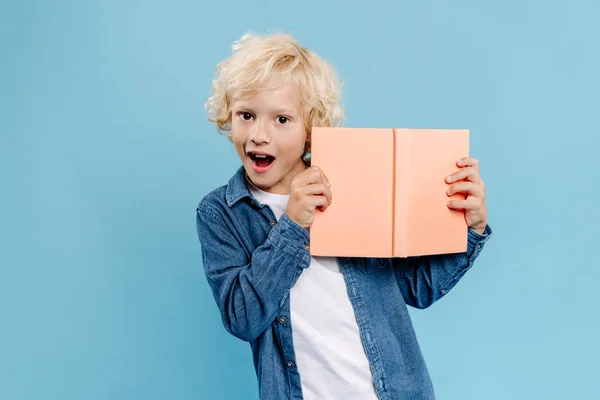 Chocado Lindo Niño Sosteniendo Libro Mirando Cámara Aislada Azul —  Fotos de Stock