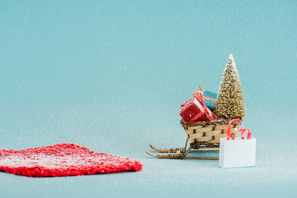красная дорожка и плетеные сани с елкой и подарочные коробки на голубом фоне
 