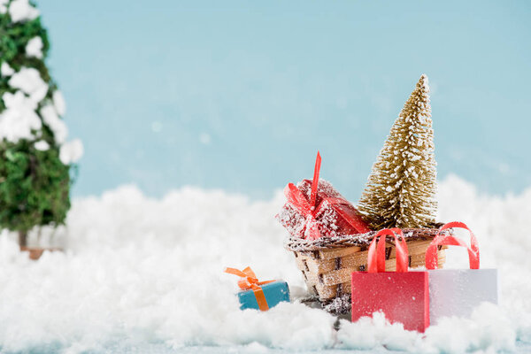 gift boxes and christmas tree in wicker sled, shopping bags in snow 