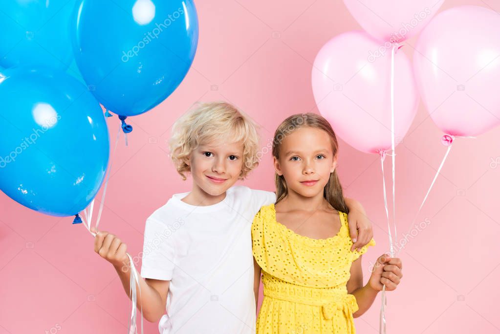 smiling and cute kids hugging and holding balloons on pink background 