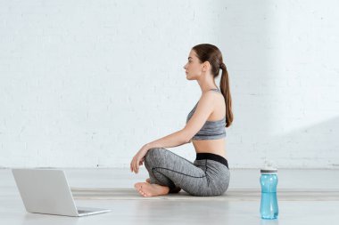 Spor kıyafetleriyle yoga yapan genç bir kadının yan görüntüsü.