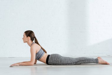 Sfenks pozisyonunda yoga yapan spor kıyafetli genç bir kadının yan görüntüsü.