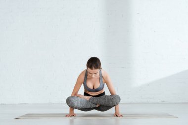 Spor kıyafetli genç bir kadın yüksek lotus pozisyonunda yoga yapıyor.