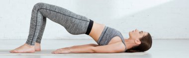 Spor kıyafetli genç bir kadın yukarı tahta duruşuyla yoga yapıyor.