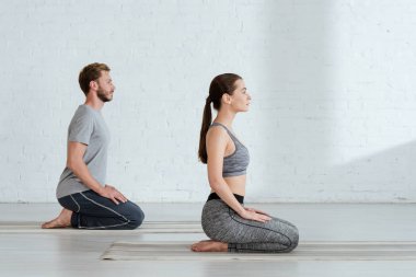 Gök gürültüsü pozisyonunda yoga yapan genç bir adam ve kadının yan görüntüsü