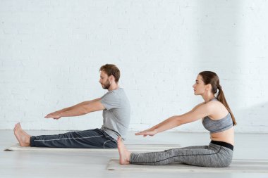 side view of man and woman practicing yoga in seated forward bend pose clipart