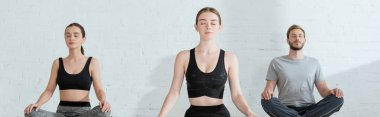 Genç erkek ve kadının yarım lotus pozuyla yoga yaptığı panoramik bir çekim.
