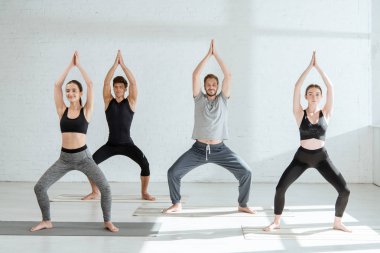  Spor kıyafetli genç insanlar Tanrıça pozisyonunda yoga yapıyorlar. Dua eden ellerle.