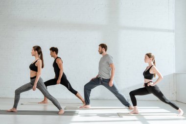 Spor kıyafetli gençlerin yan görünüşü Savaşçı pozunda yoga yapıyor.