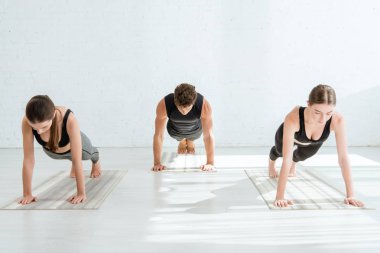 Genç kadınlar ve erkek tahta duruşunda yoga yapıyorlar.