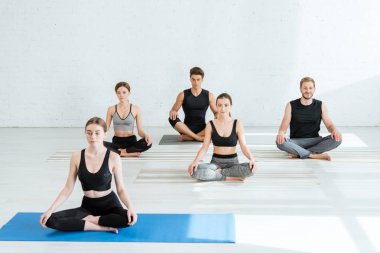 Beş genç, yarım lotus pozuyla yoga yapıyor.