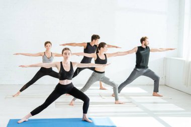 5 genç erkek ve kadın savaşçı pozisyonunda yoga yapıyorlar. 