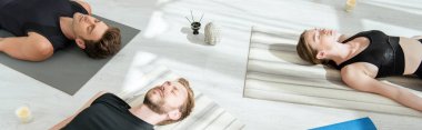 Genç insanların cesette meditasyon yaparken panoramik çekimleri dekoratif Buddha kafası, aromatik çubuklar ve mumların yanında poz veriyor.