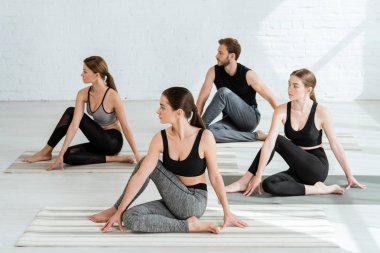 Spor merkezinde, omurga bükme pozisyonunda yoga yapan dört genç insan.