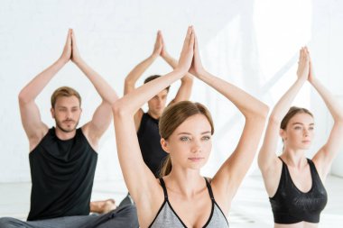 Spor giyimli gençler, dua eden ellerle yoga yapıyorlar.