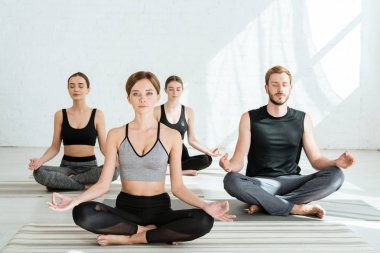 front view of young people practicing yoga in half lotus pose clipart