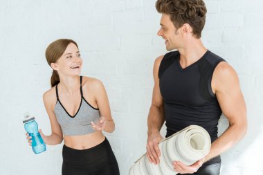 Spor şişeli neşeli kadın yoga minderi tutan adama gülümsüyor.