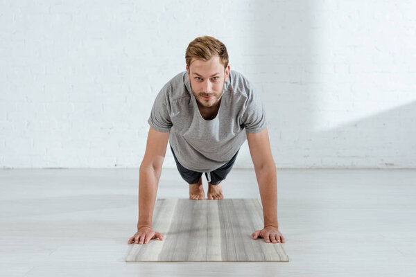 handsome man looking at camera while practicing plank pose