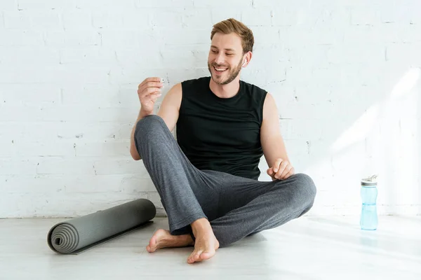 Glad Man Sitter Golvet Nära Yogamatta Och Sportflaska Och Håller — Stockfoto