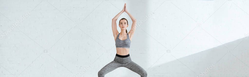 panoramic shot of young woman in sportswear practicing yoga in goddess pose with raised prayer hands