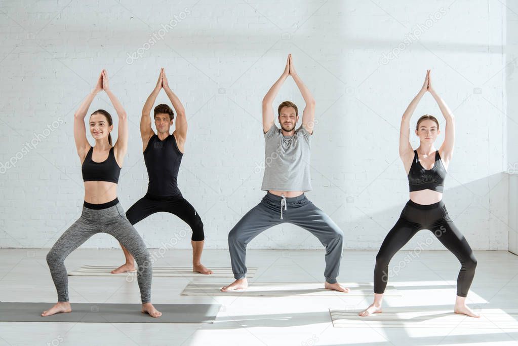  young people in sportswear practicing yoga in goddess pose with raised prayer hands