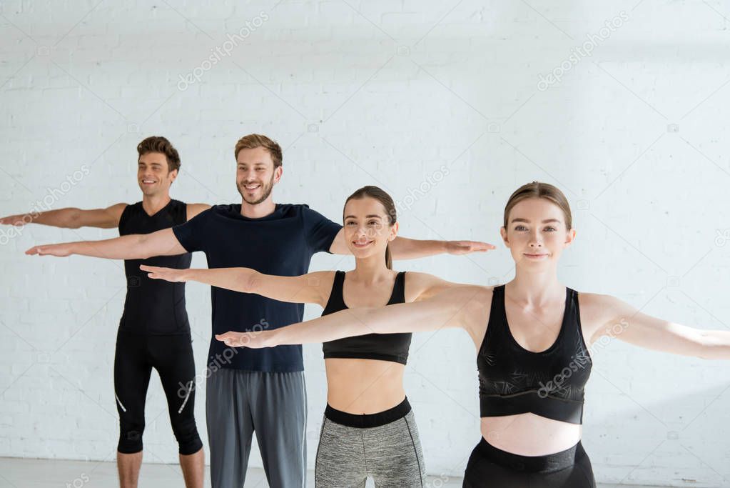 smiling young people in sportswear practicing yoga in mountain open arm pose