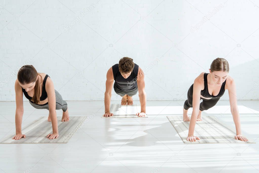 young women and man practicing yoga in plank pose