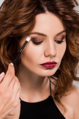 cropped view of makeup artist apply eye shadow on beautiful woman isolated on grey  clipart