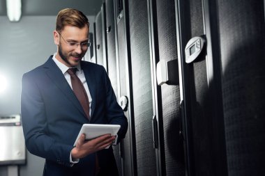 Veri merkezinde dijital tablet kullanan takım elbiseli neşeli iş adamının seçici odağı 