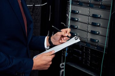 cropped view of man in suit holding clipboard and pen in data center  clipart