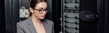 panoramic shot of attractive businesswoman in glasses near server rack in data center  clipart