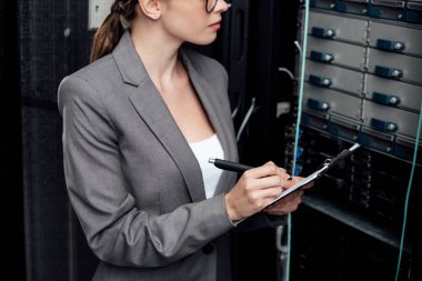 cropped view of businesswoman holding clipboard and pen in data center  clipart