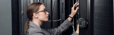 panoramic shot of businesswoman in glasses looking at server rack in data center  clipart