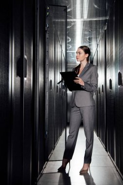 beautiful businesswoman holding clipboard while standing in data center  clipart