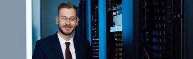 panoramic shot of businessman in glasses smiling in data center  clipart