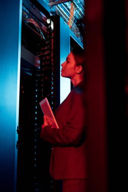 selective focus of attractive businesswoman looking at server rack and holding digital tablet  clipart