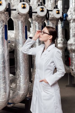 Beyaz önlüklü çekici bir mühendis el ele tutuşup hava sıkıştırılmış sisteme bakarken gözlüklere dokunuyor. 