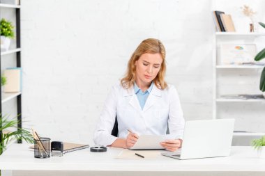 Çekici beslenme uzmanı masada oturup klinikte kağıda yazı yazıyor. 