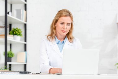 Çekici beslenme uzmanı masada oturuyor ve klinikte dizüstü bilgisayar kullanıyor. 