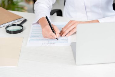 cropped view of nutritionist sitting at table and filling in medical card in clinic  clipart