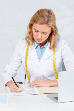 Çekici beslenme uzmanı masada oturup klinikte kağıda yazı yazıyor. 