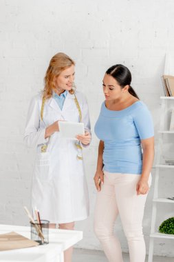 Klinikteki hastaya dijital tablet gösteren çekici beslenme uzmanı 