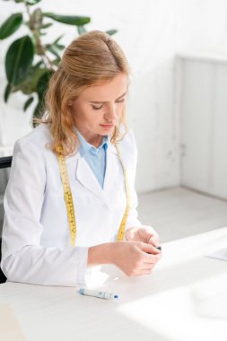 Çekici beslenme uzmanı masada oturuyor ve klinikte glukometre tutuyor. 
